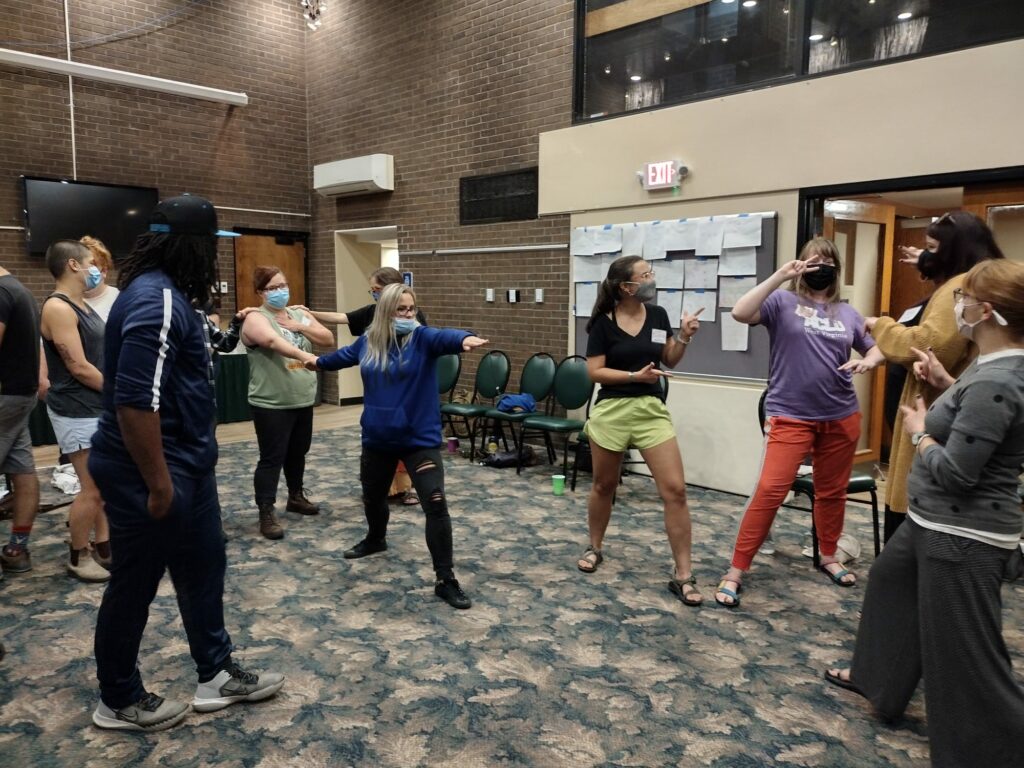 A group of standing masked workshop participants making intentional poses during a training.